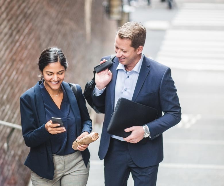 A man and woman look at a mobile phone while coming up a flight of stairs.
