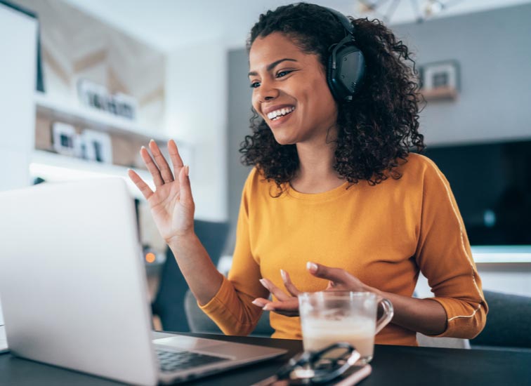 A woman wearing a headset talks to others on her laptop.