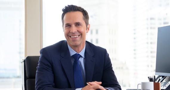 A smiling businessman seated behind a desk.
