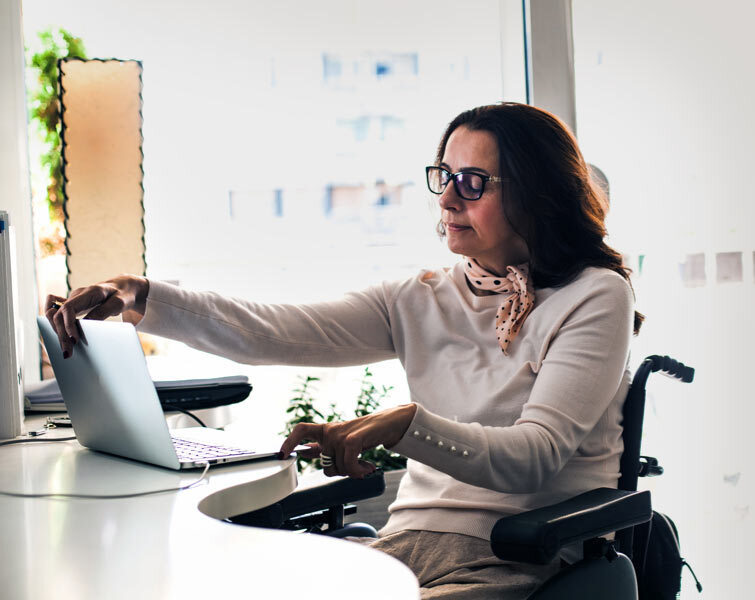 A woman in a wheelchair opens her laptop computer.