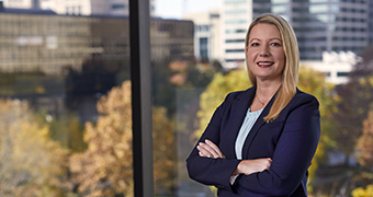 A female Edward Jones Associate standing by an office window overlooking trees and other buildings.