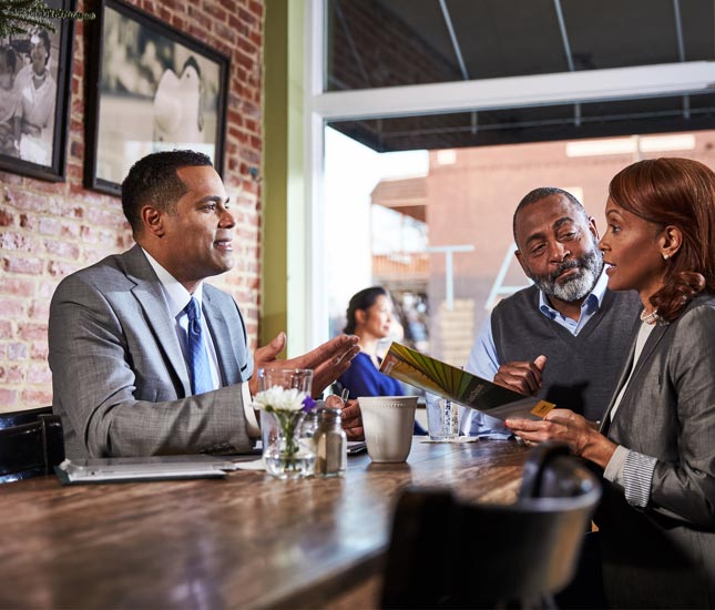 Un représentant en services financiers assis à une table de restaurant parle à un couple.