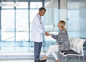 Une patiente dans une salle d’attente rencontre un clinicien masculin en blouse blanche et lui serre la main.
